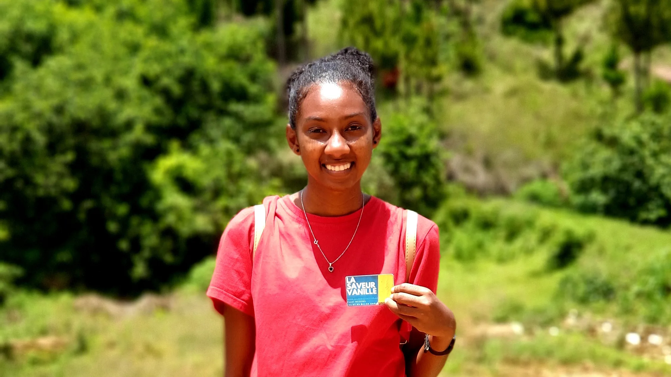 Young woman in a forest holding a card with the inscription LA SAVEUR VANILLE, symbolizing the company's commitment to nature and the quality of Madagascar vanilla.